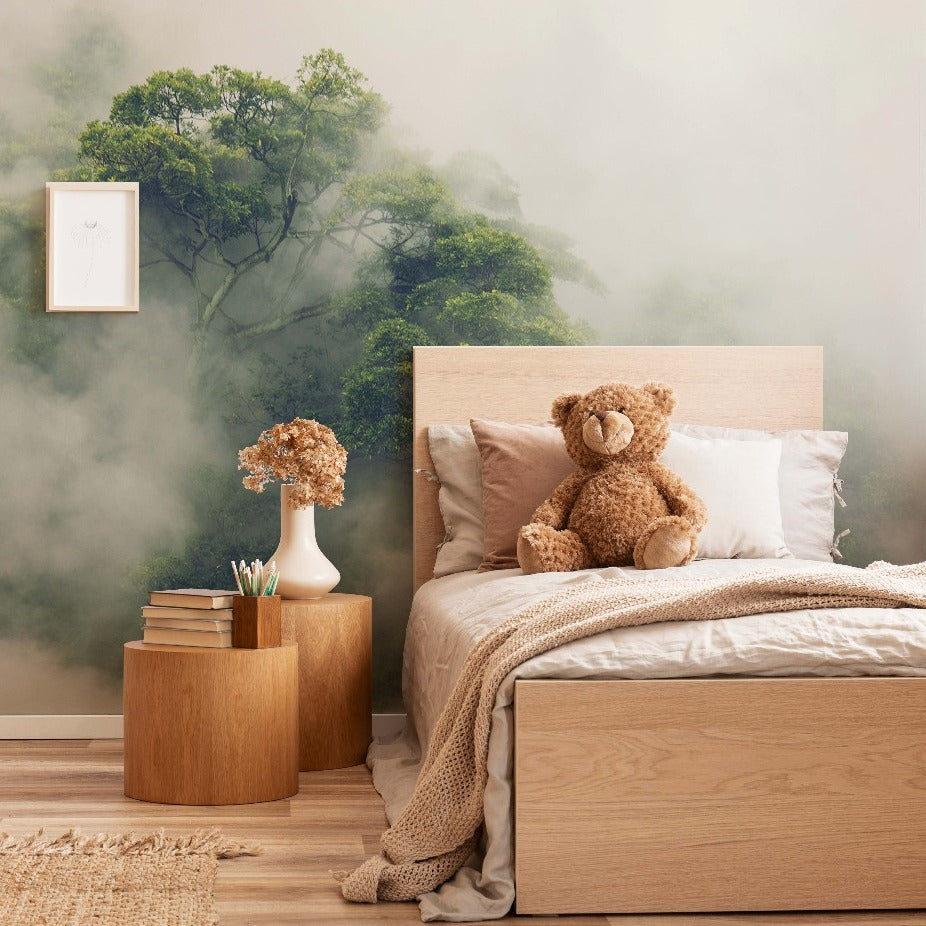 Bedroom - A cozy bedroom featuring a wooden bed with beige and gray linens, a teddy bear sitting on the bed, and a round wooden bedside table with books and a vase of flowers. The wall has Decor2Go Wallpaper Mural's Hidden Tree Wallpaper Mural.