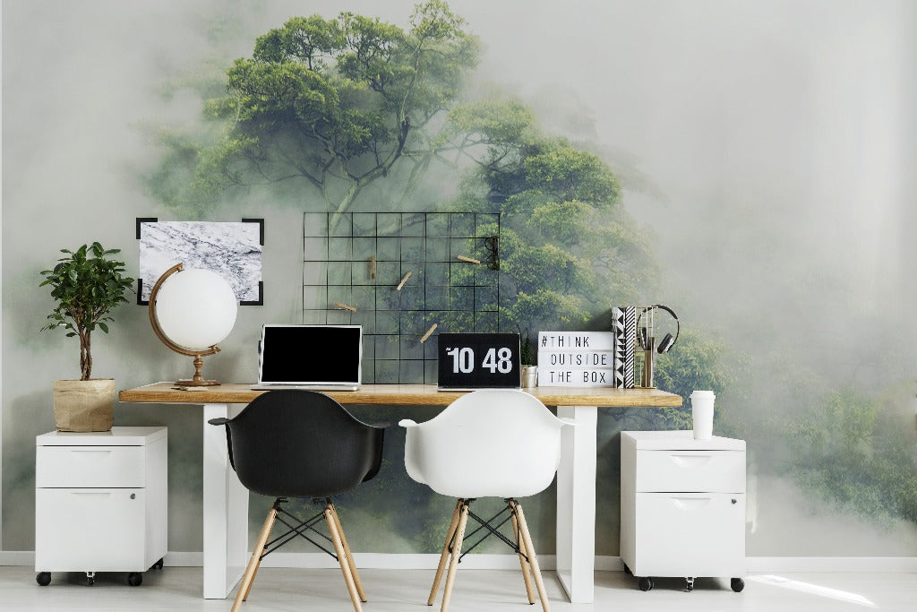 A modern home office with a wooden desk, two white chairs, a laptop, decorative items, and a large Decor2Go Wallpaper Mural of a green, misty forest.