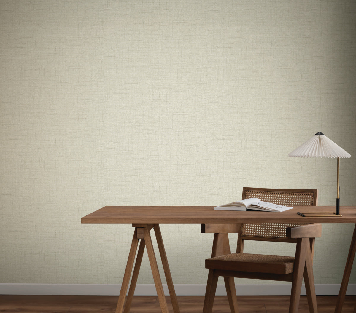 A wooden desk, open book, pleated-shade lamp, and wooden chair sit before York Wallcoverings’ Hillswick Tweed Beige Wallpaper (60 SqFt), creating a minimal, modern look.