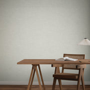 Home Office - A minimalist with a wooden desk, chair, and a white pleated lamp sits against a backdrop of York Wallcoverings’ Hillswick Tweed Pewter Wallpaper (60 SqFt), adding subtle texture and warmth to the room