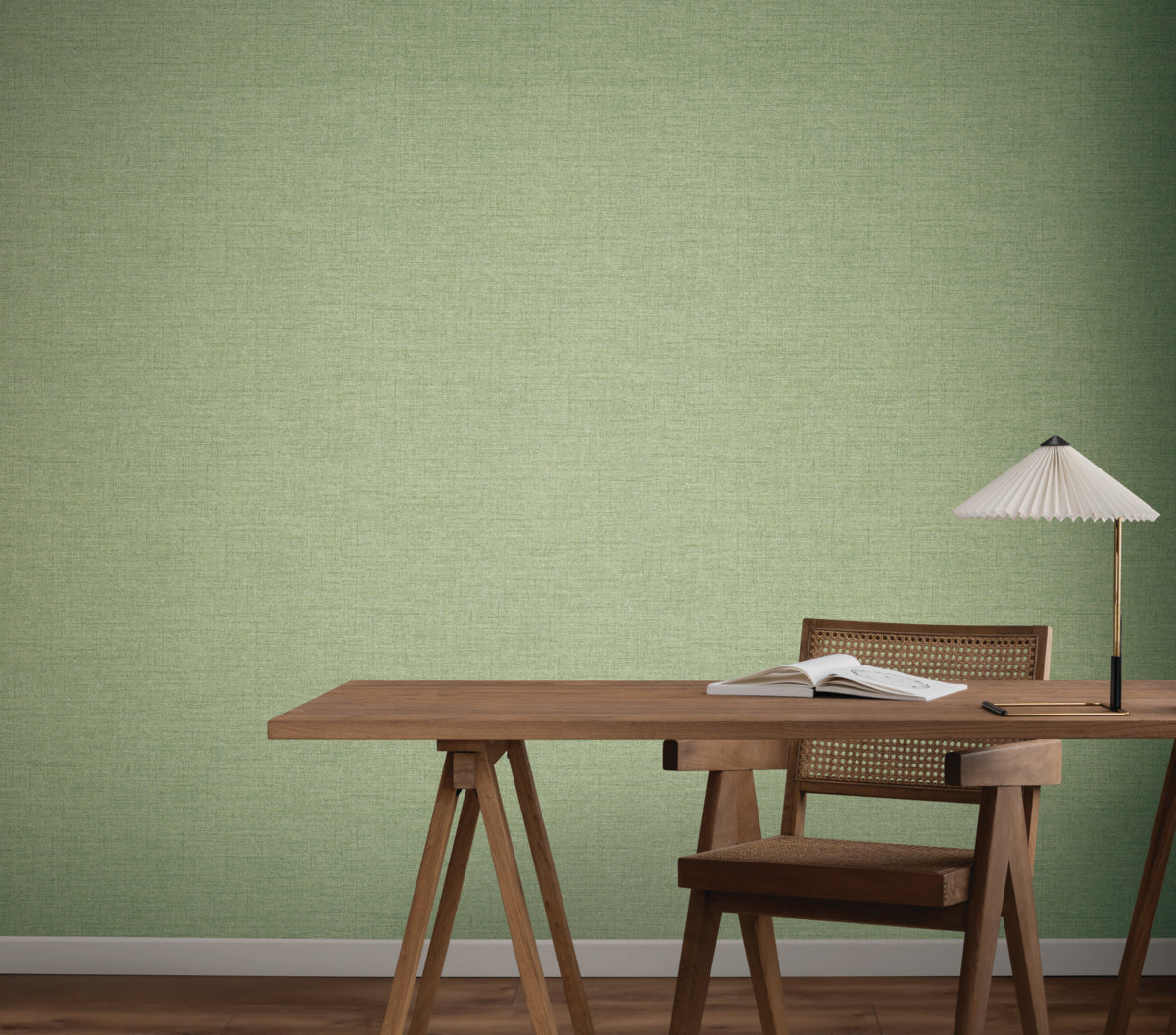 A wooden desk with an open book and table lamp sits against a wall covered in Hillswick Tweed Shamrock Wallpaper by York Wallcoverings. A wooden chair with a woven back is at the desk, and the floor is brown wood.