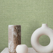 Three decorative vases sit on a light surface against York Wallcoverings' Hillswick Tweed Shamrock Wallpaper, featuring a vibrant spring green hue; the vases include a tall marbled piece, a small round one, and a large hollow-centered design.