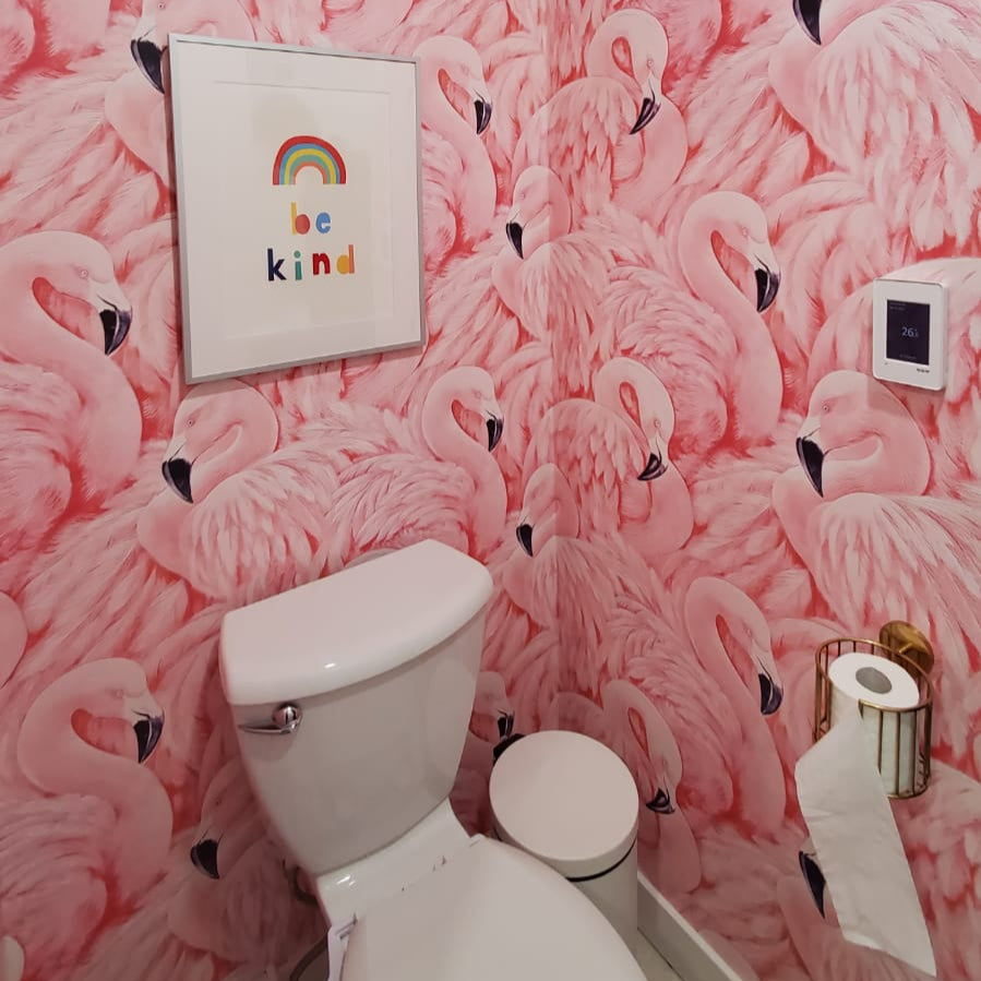 Bathroom - A small bathroom with Decor2Go Wallpaper Mural's Pink Flamingos Mural exudes a Tropical Escape vibe. A framed rainbow "be kind" print hangs above the white toilet, adding charm. A toilet paper holder on the right wall completes the Coastal Charm.