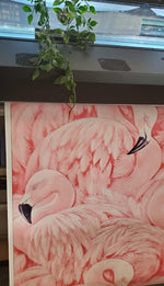 The Decor2Go Wallpaper Mural features a detailed Pink Flamingos Mural Wallpaper, propped against a cabinet under a window, exuding coastal charm. A leafy green plant trails down from above, highlighting the intricately depicted soft feathers of the flamingos.