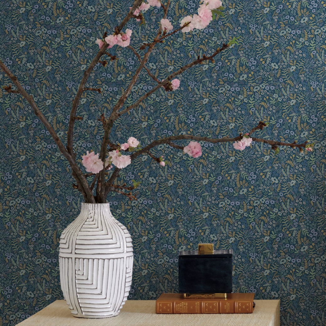 A white vase with geometric patterns holds blossoming branches on a table beside two stacked books and a small black box. The background showcases York Wallcoverings' Indigo Tapestry Wallpaper (60 SqFt), adding a botanical blue touch.