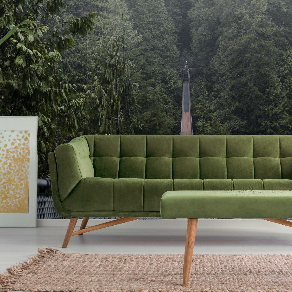 A modern green velvet sofa on a beige rug, with a white frame containing abstract art on the left, in front of an Into the Woods Wallpaper Mural seen through large windows.