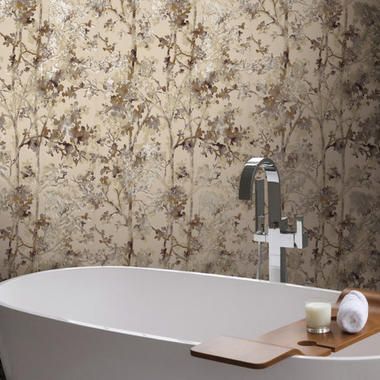 A modern bathroom features a white freestanding bathtub with a wooden tray holding a candle and rolled towel. The Khaki & Multi Shimmering Foliage Wallpaper by York Wallcoverings, in shades of beige and brown, adds elegance alongside elements from the Modern Metals Collection.