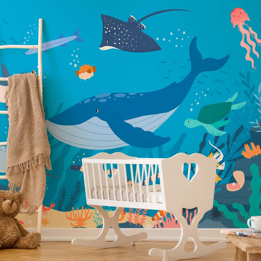 A colorful nursery room with an educational tool, the "Decor2Go Wallpaper Mural" featuring a large blue whale, stingray, and various sea creatures. Beside it, a white crib and rocking.