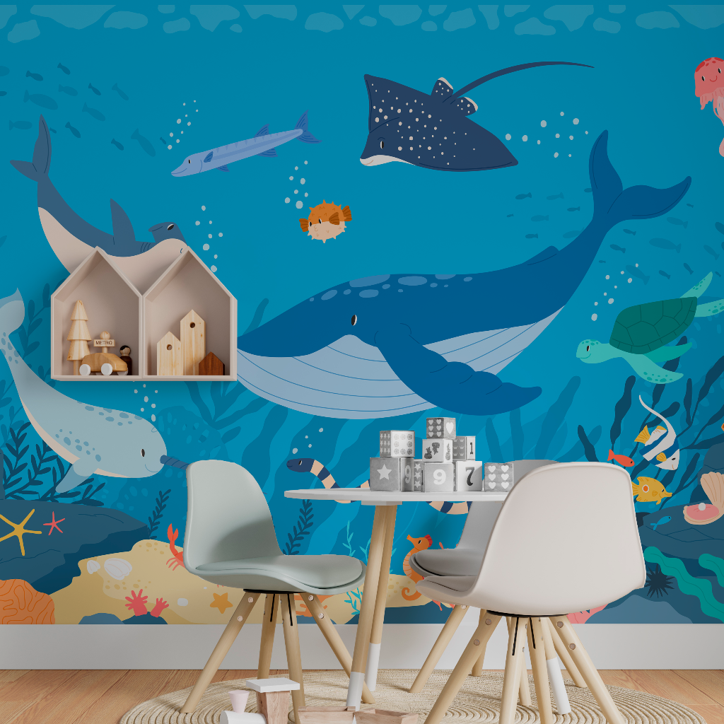A children's playroom with a vibrant Decor2Go Wallpaper Mural featuring large illustrations of whales, fish, and other sea creatures. A small table with chairs and toys is set in the foreground.