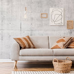 A stylish living room featuring a modern grey sofa with decorative brown pillows, set against a Decor2Go Wallpaper Mural with minimalist art and hanging geometric lights. A woven basket sits by the sofa.