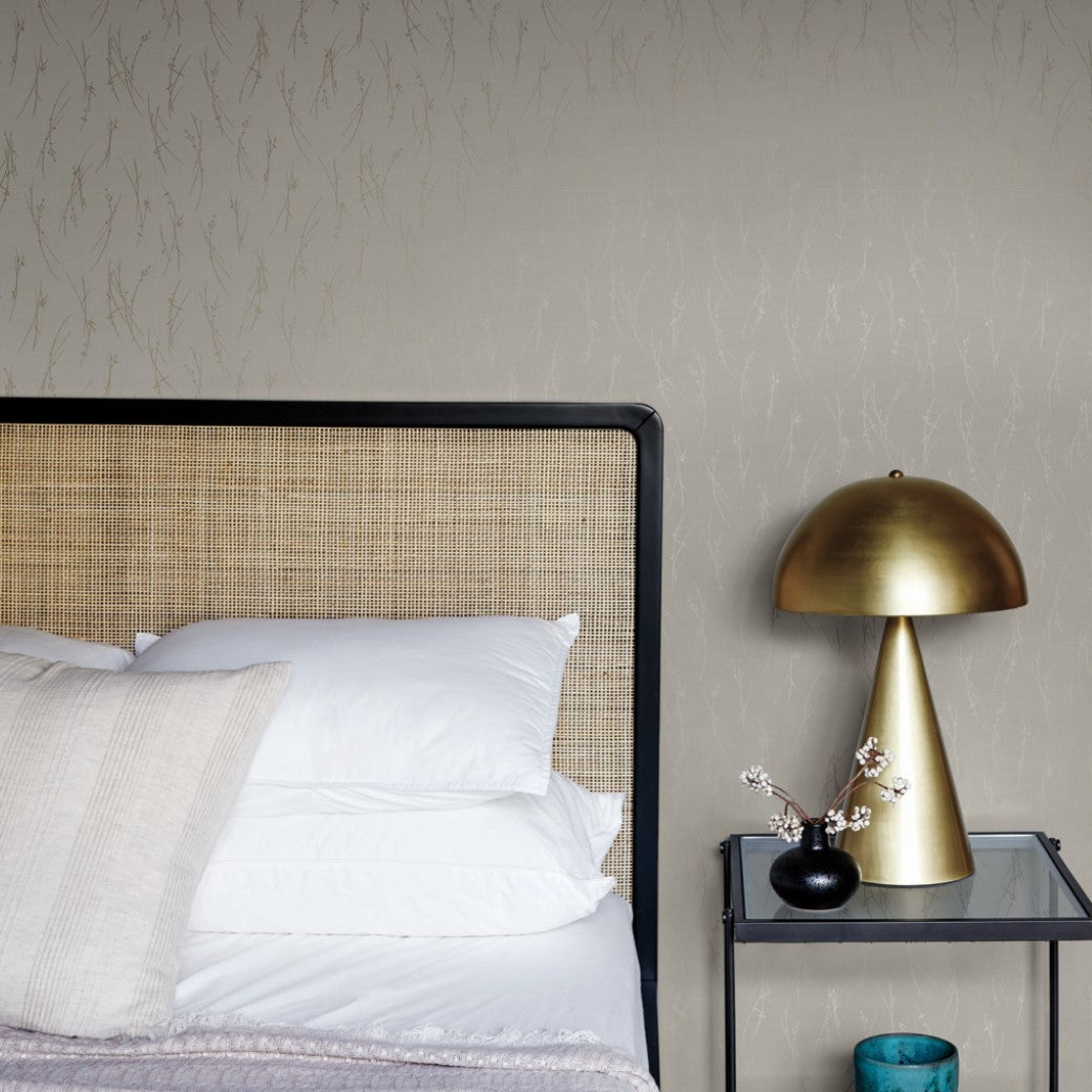 Bedroom - A modern showcases a wicker-backed bed with white pillows and a lavender throw. A sleek nightstand holds a gold lamp, complementing a small branch in a vase. The standout feature is the York Wallcoverings' Light Grey & Gold Sprigs Wallpaper, providing a textured elegance to the wall