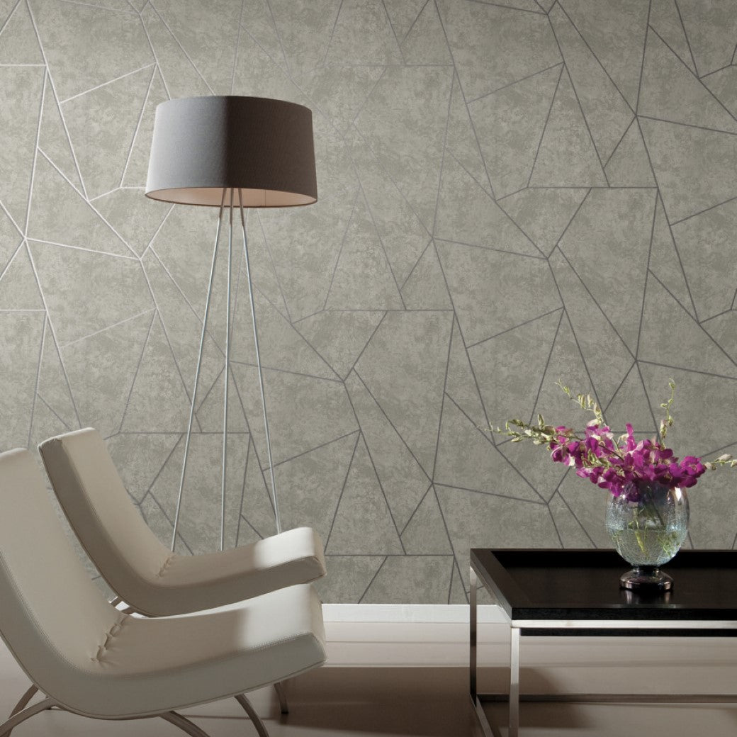 The room showcases two white armchairs, a dark rectangular side table with a vase of purple flowers, and a tall floor lamp. The York Wallcoverings Light Grey & Silver Nazca Wallpaper enhances the geometric design with gray lines on a textured surface for added depth and style.