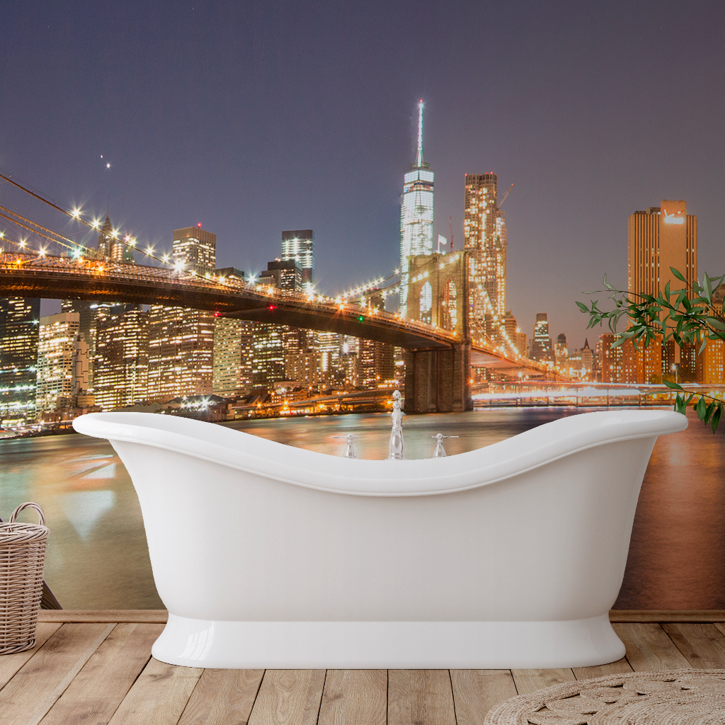 A luxurious freestanding bathtub on a wooden floor, with a view of the New York City skyline and Brooklyn Bridge at night through a large panoramic window featuring Decor2Go Wallpaper Mural.