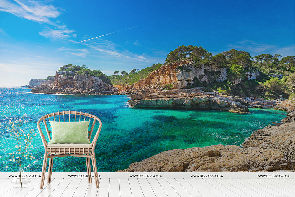 A serene view from a white deck featuring a single turquoise chair with a light green cushion overlooking a vibrant Decor2Go Wallpaper Mural sea, surrounded by rocky cliffs and lush green trees under a clear sky.