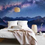 Bedroom - A luxurious bedroom with a large white bed draped with a beige blanket. The room features a stunning Milky Way Mountains Wallpaper Mural from Decor2Go Wallpaper Mural. Wicker lamps add a cozy ambiance.