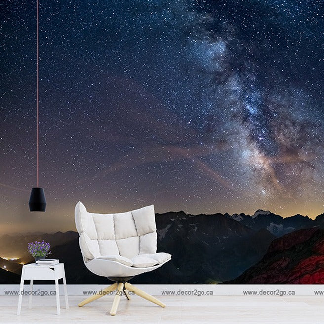 A stylized room with an armchair and hanging lamp overlooking a digitally enhanced view of a mountainous landscape under a Decor2Go Milky Way Wallpaper Mural.