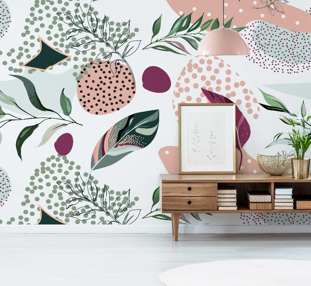 A stylish interior with a Millenial Collage Wallpaper Mural by Decor2Go featuring abstract patterns and plants. A wooden credenza with framed art and decorative objects is under a trendy pink lamp.