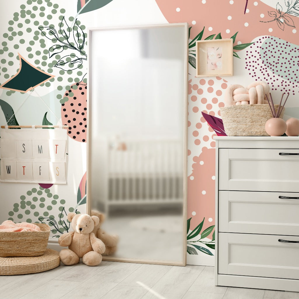 A colorful nursery with a playful Decor2Go wallpaper mural, featuring a white dresser, a mirror, a basket with toys, and teddy bears on the floor. A reflection of a crib is visible in the mirror.