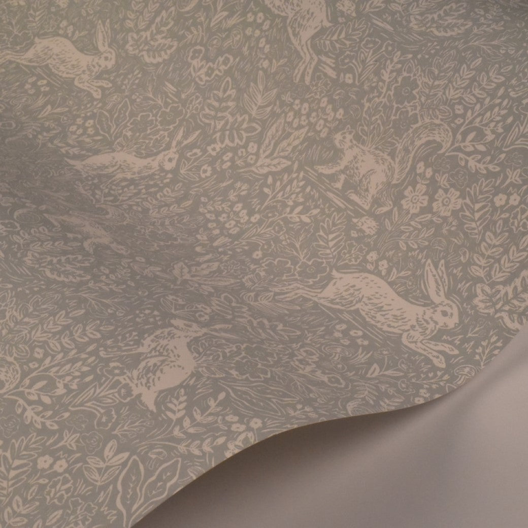 Mineral Fable Wallpaper (60 SqFt) by York Wallcoverings features a delicate pattern of white rabbits, flowers, and leaves on a light gray background, reminiscent of Rifle Paper Co. Fable Wallpaper. Slight curve at one corner.