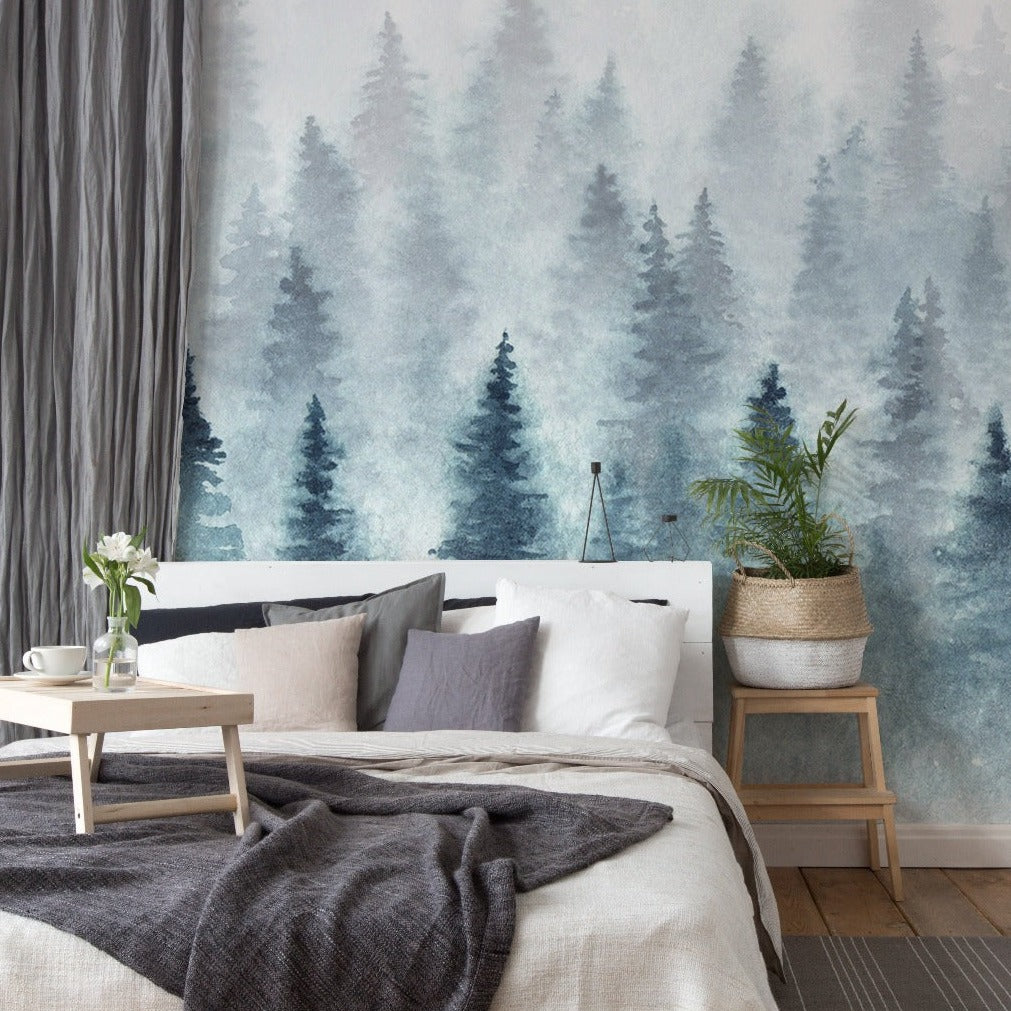 A serene bedroom with a Decor2Go Wallpaper Mural featuring silhouettes of pine trees. The room includes a bed with gray and white bedding, a small wooden table, and a potted