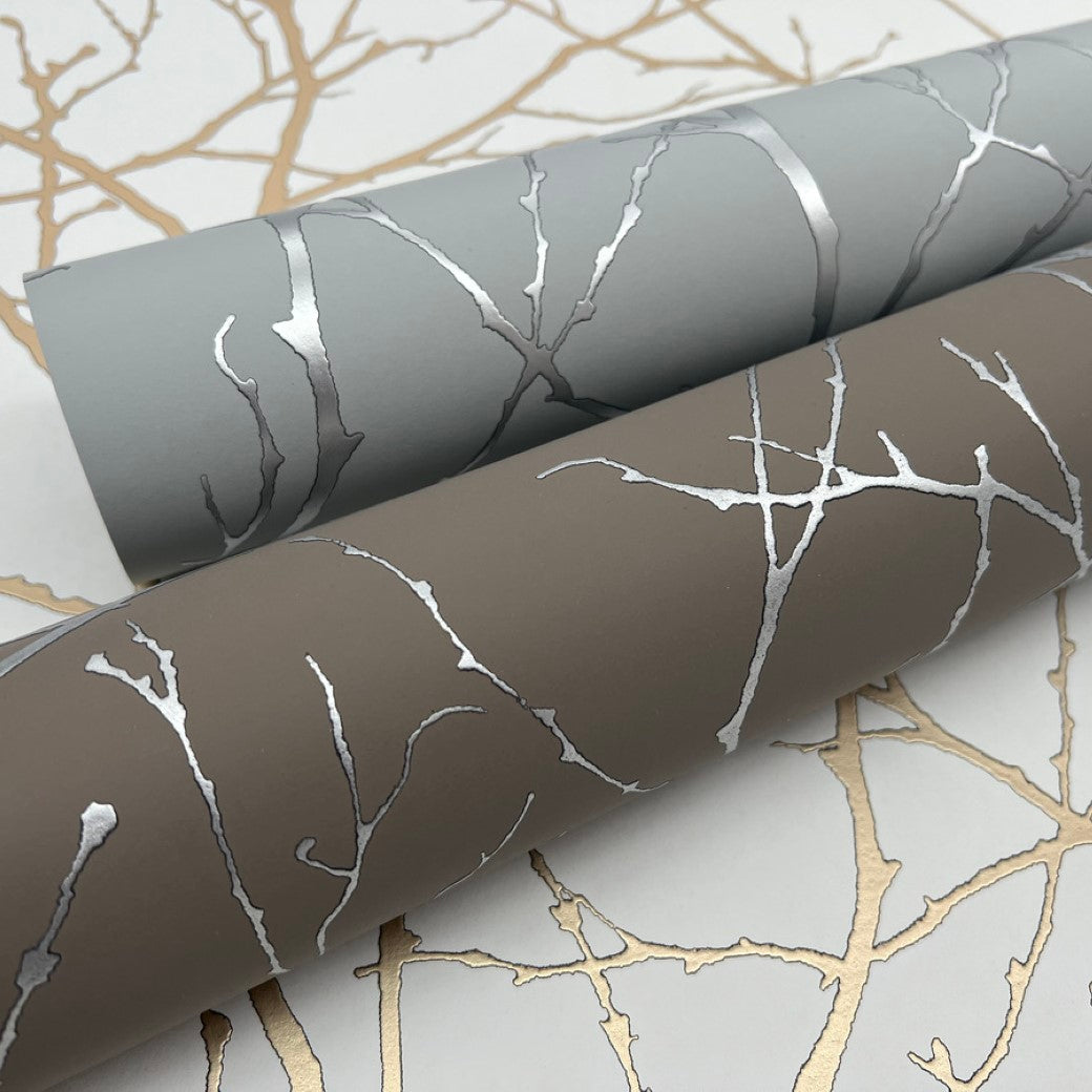 The Mocha & Silver Trees Silhouette Wallpaper by York Wallcoverings features a captivating design of metallic tree branches in silver, with one roll in gray and the other in brown, each emphasizing intricate silhouettes over a matching background. Each roll covers 57 SqFt.