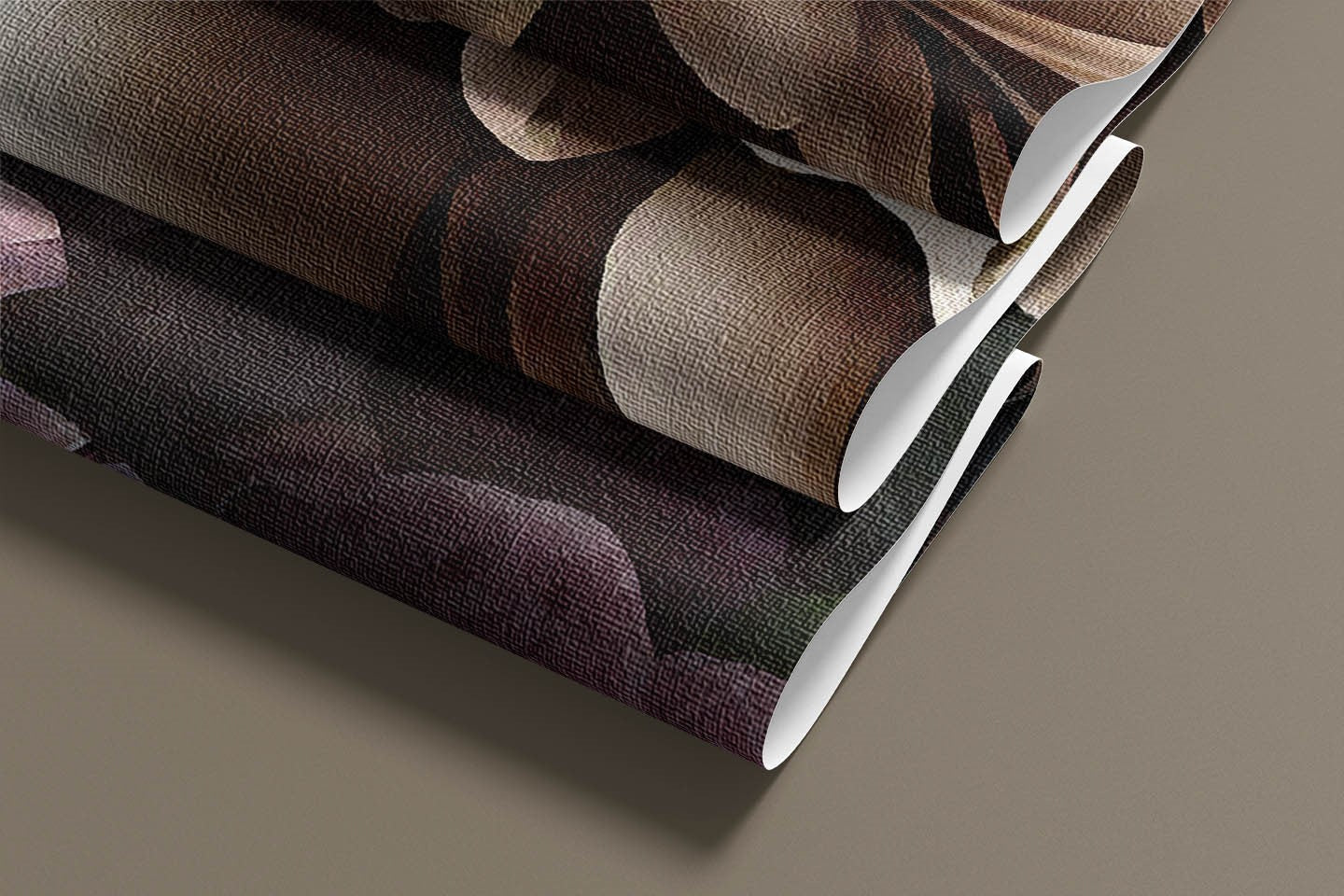 Close-up of three rolls of Decor2Go's "Moody Floral Elegance" wallpaper mural, showcasing abstract designs in brown, black, and purple hues that exude a dark sophisticated ambiance as they rest on a gray surface.