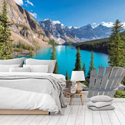 Bedroom - A modern bedroom with an open wall featuring a Decor2Go Wallpaper Mural of Moraine Lake surrounded by forested mountains. The room includes a neat bed, side table, chair, and a