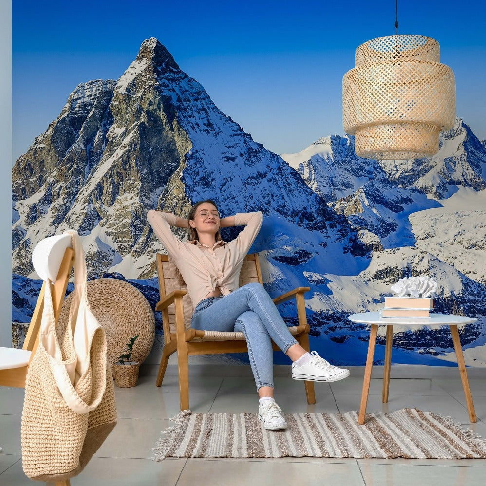 A woman sitting in a chair in front of a mural of the Mountain Tops mountain range - Decor2Go Wallpaper Mural.