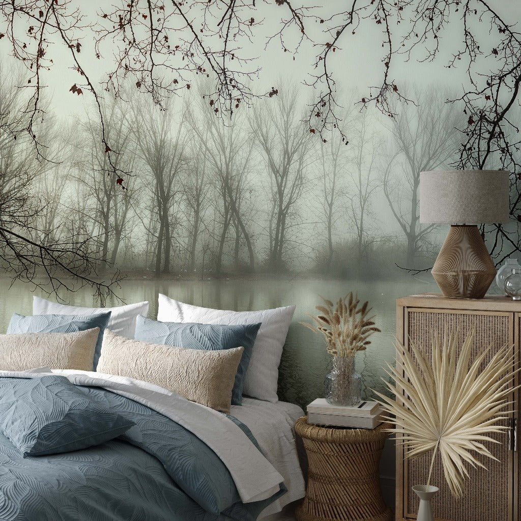 A cozy bedroom featuring a neatly made bed with blue and white bedding, beside a wooden nightstand and lamp. The room overlooks a serene, foggy forest landscape through a large Decor2Go Wallpaper Mural.