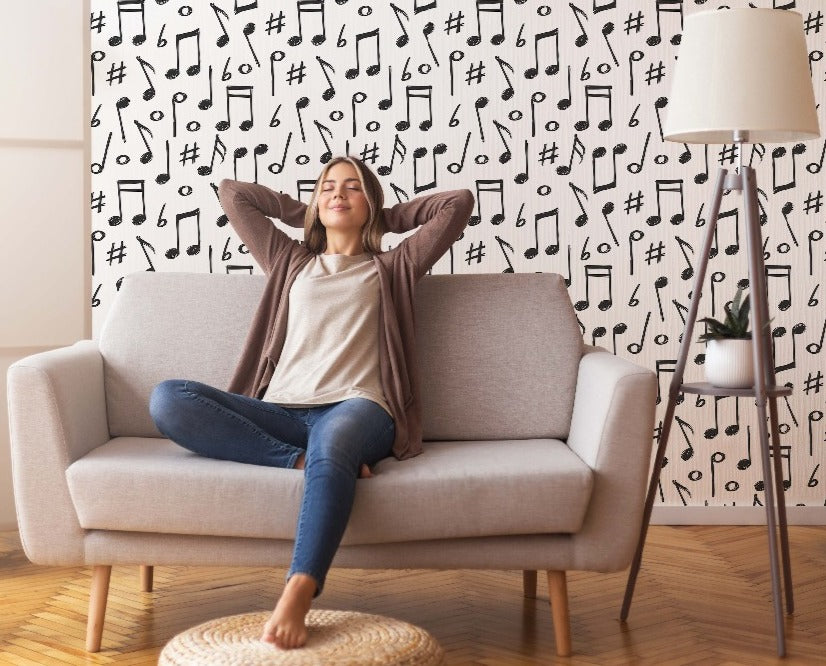 A relaxed woman sits on a sofa with her arms stretched behind her head, smiling with closed eyes, in a living room decorated with Decor2Go Wallpaper Mural.