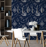 A modern dining area features a white table with white chairs on wooden legs. Decorative vases and a floral arrangement sit on the table. A Nautical Treasure Adventure Wallpaper Mural by Decor2Go Winnipeg with marine elements and three pendant lights add a stylish touch to the room. Shelves on the left hold more decorative items.