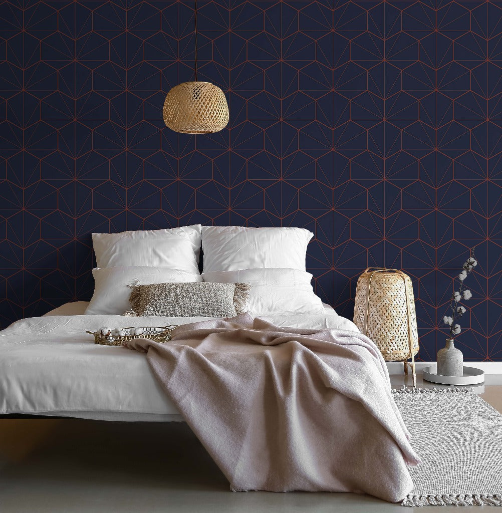 A modern bedroom featuring a bed with white bedding and a taupe throw blanket, set against a Navy and Red Hexagons Wallpaper Mural from Decor2Go Wallpaper Mural, with a wicker lamp hanging overhead and a matching bedside lamp.