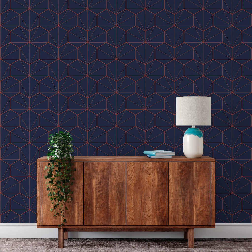 A modern living room scene featuring a wooden sideboard against a wall with Navy and Red Hexagons Wallpaper Mural from Decor2Go Wallpaper Mural. On the sideboard, there is a lamp, a hanging green plant, and two books.
