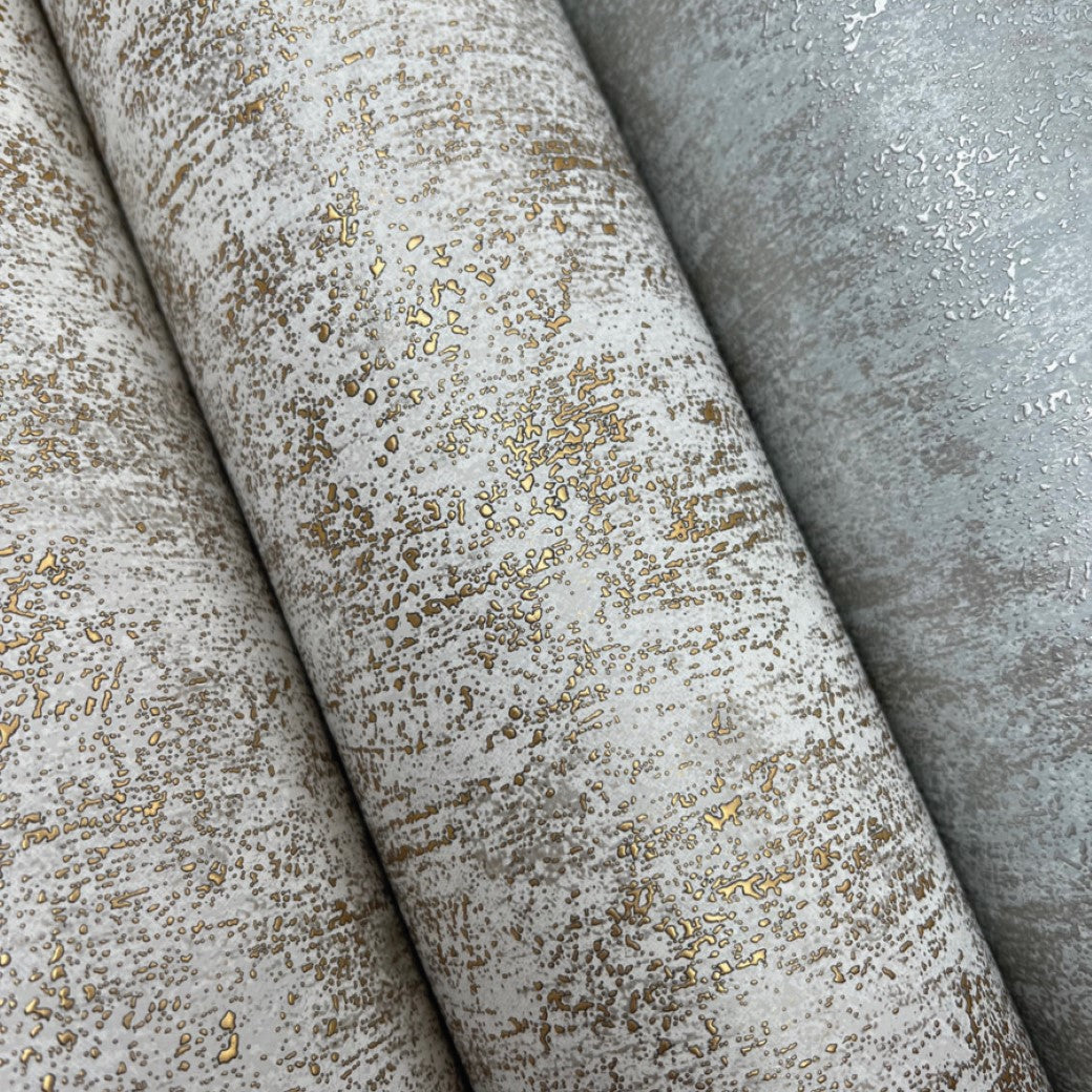 A close-up of three rolls of York Wallcoverings' Neutral & Gold Shimmering Patina Wallpaper (57 SqFt) highlights a textured, distressed design with metallic gold speckles on a white and pale gray background, ideal for contemporary interiors.