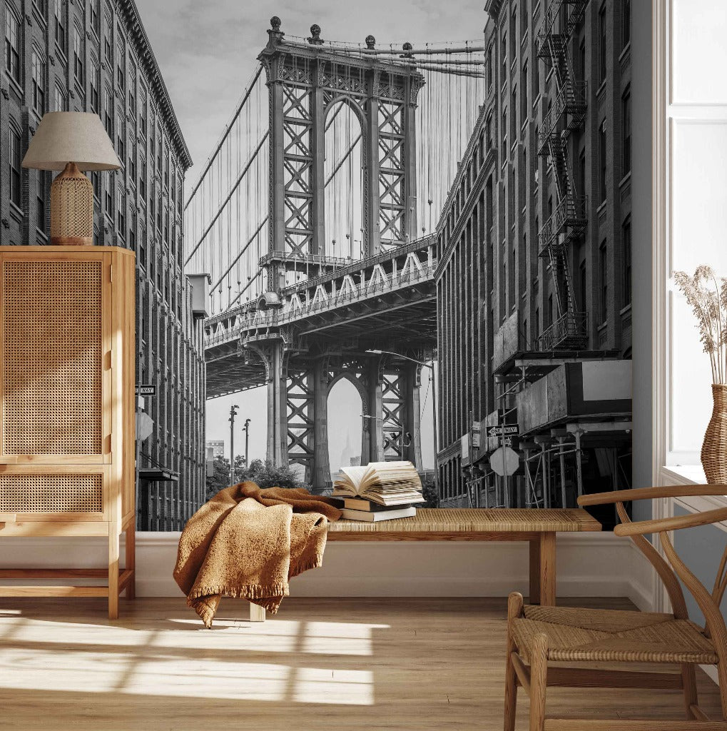 A cozy room furnished with a wooden bench, chair, and shelf, featuring a large Decor2Go Wallpaper Mural of the New York Bridge in black and white, overlooking a city street.