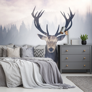 Bedroom - A modern bedroom featuring a large outdoor mural of an Oh Deer! with expansive antlers, set against a misty forest backdrop. The room includes a neatly made bed and a grey dresser adorned with plants from Decor2Go Wallpaper Mural.