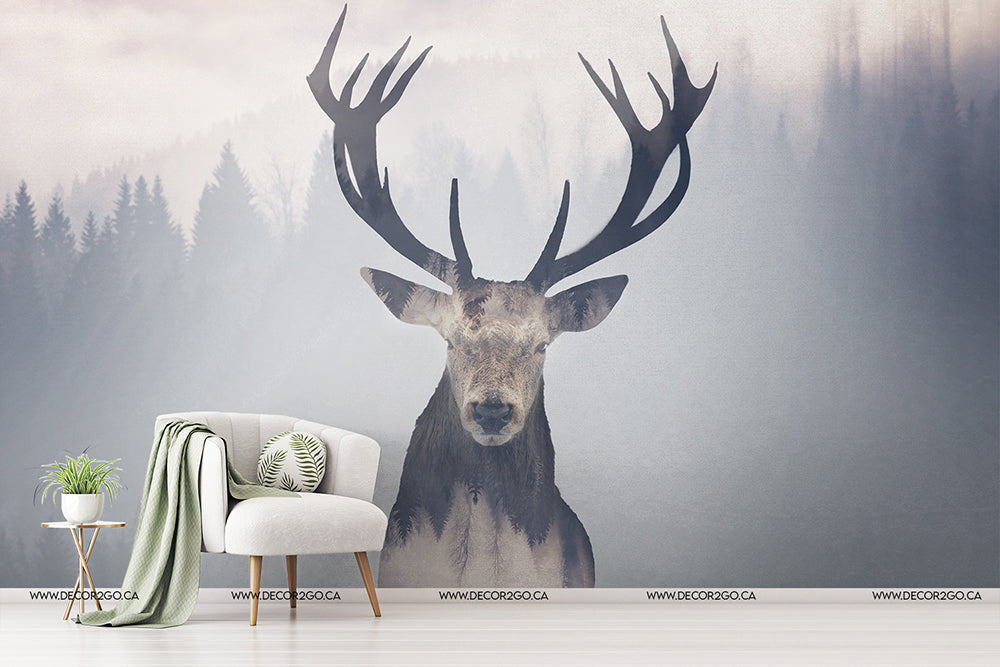 A modern living room corner featuring a white chair with a green blanket and pillows next to a small white side table with plants, against an Oh Deer! wallpaper mural of a large stag with expansive antlers set against Decor2Go wallpaper mural.