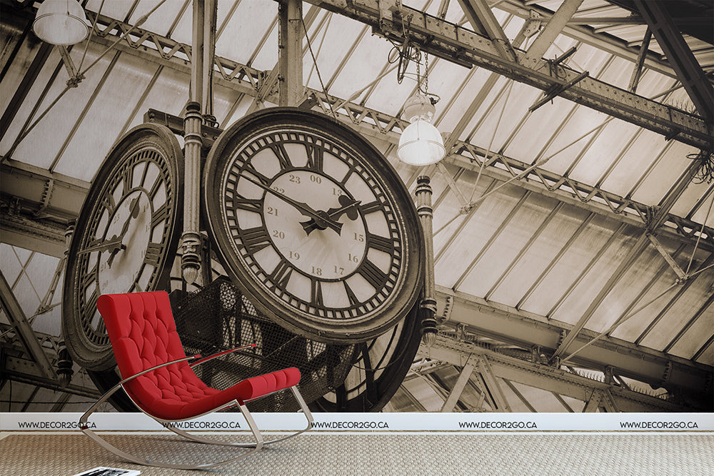 A stylish red lounge chair sits under a large, ornate On time Clockwork Wallpaper Mural mounted on an iron beam in a station with a glass and metal roof overhead, perfect for taking a break.
