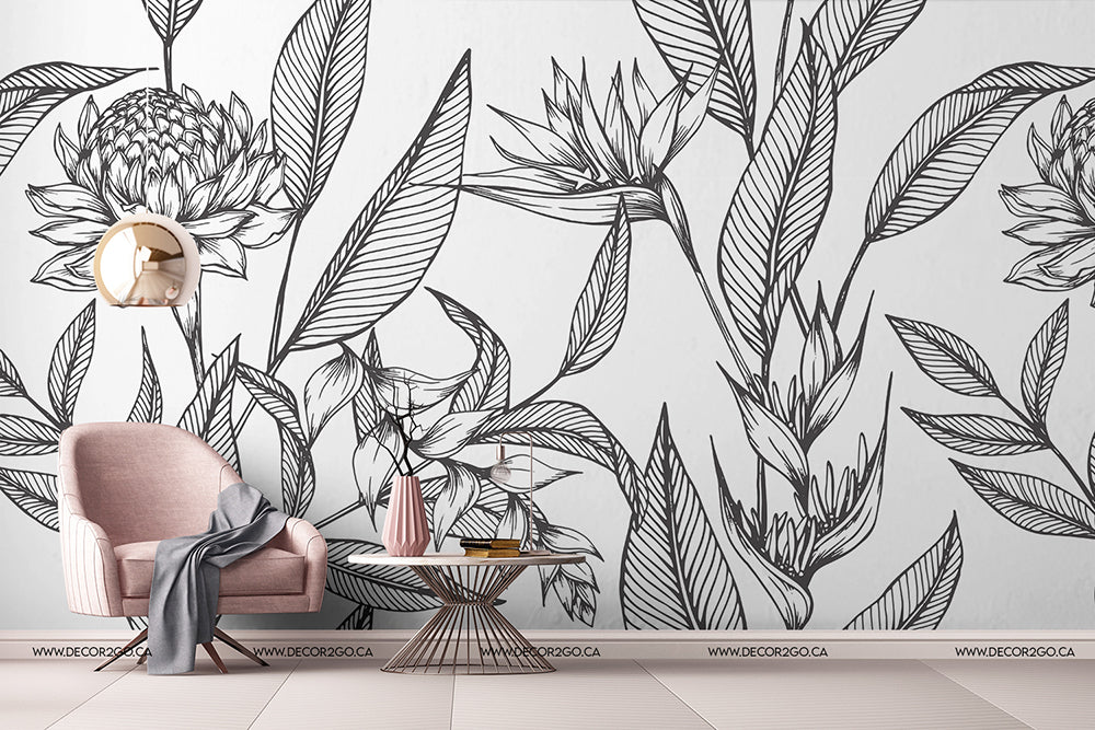 A stylish living room with white walls featuring large, black Decor2Go Paradise Flower Wallpaper Murals. There's a pink armchair with a gray throw, a round coffee table, and a wall clock with a unique design.