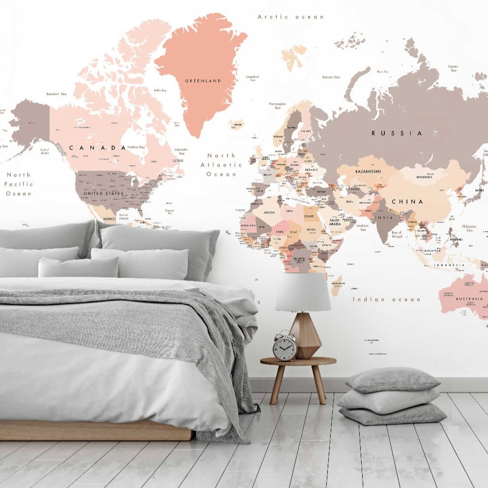 A modern bedroom with a large Decor2Go Peach World Map Wallpaper Mural in pastel colors. The room includes a neatly made bed, a wooden bedside table with a clock, and a gray cushion on the floor.