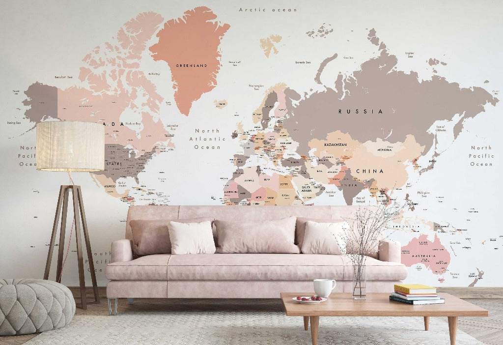 A modern living room featuring a soft pink sofa with cushions, Peach World Map Wallpaper Mural on the wall, a standing lamp, and a small coffee table with books and a cup.