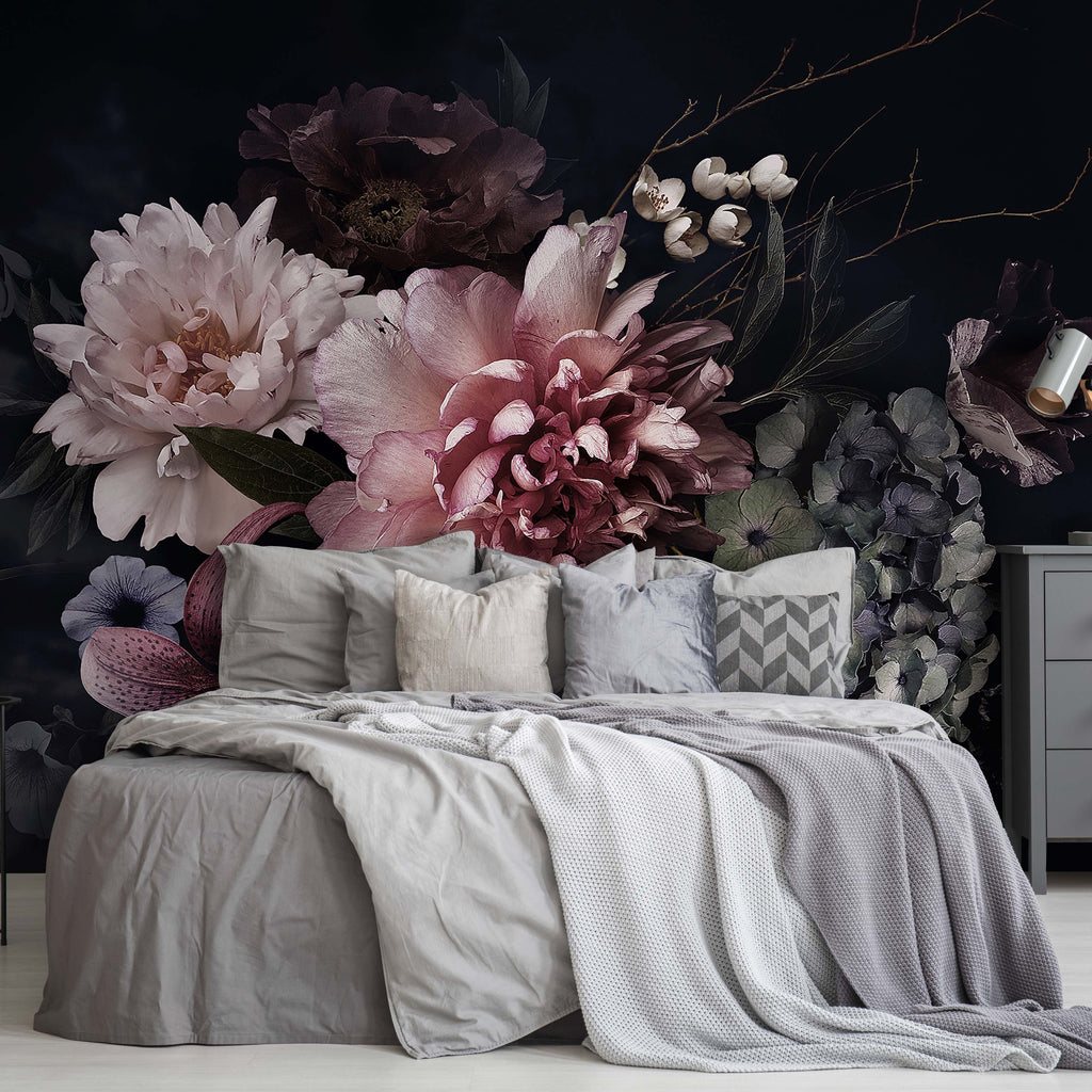 A stylish bedroom featuring a large bed with gray and beige bedding, a massive Peonies Over Black Wallpaper Mural from Decor2Go behind it, and a gray dresser with a lamp and plant.
