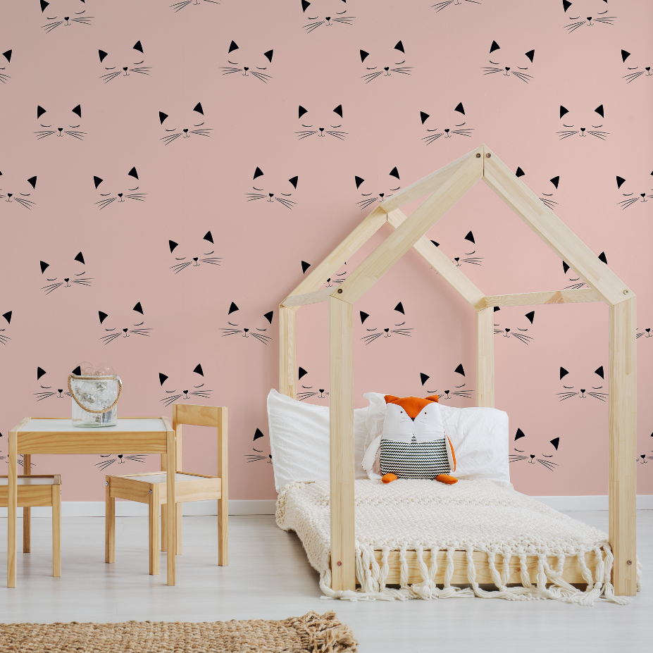 A cozy children's bedroom featuring a wooden house-framed bed with white bedding, wood table and chairs, and a pink wall adorned with a Decor2Go Wallpaper Mural.