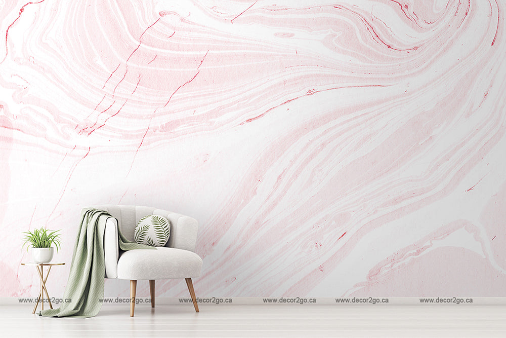 A minimalist living room with a stylish white armchair adorned with a green throw and cushion next to a small plant on a table, set against a large Decor2Go Pink Marble Wallpaper Mural wall.