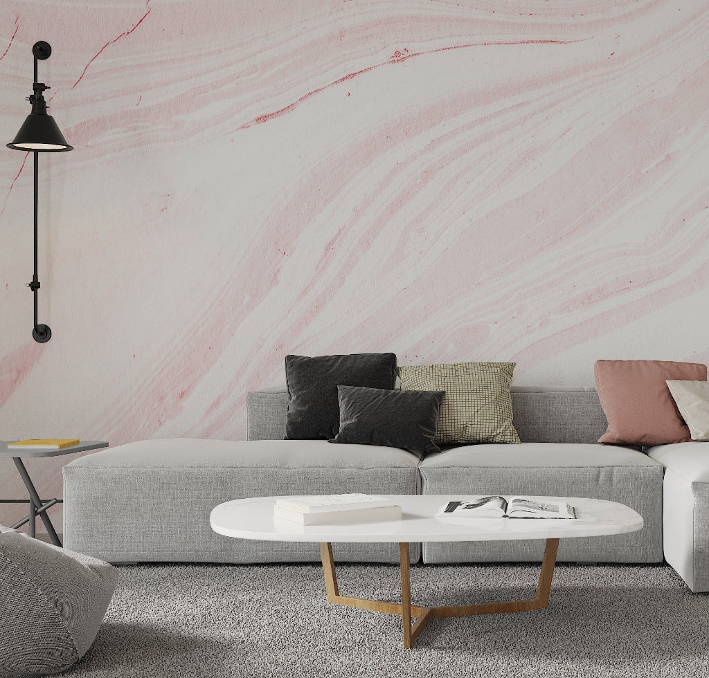 A modern living room with a gray sofa adorned with various cushions, a round white coffee table with books on it, a hanging black lamp, and a Decor2Go Wallpaper Mural Pink Marble Wallpaper Mural background.