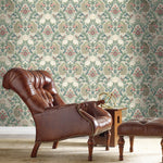 A vintage leather armchair and matching ottoman are placed in front of Plume Dynasty Peacock & Floral Wallpaper - Taupe/Multi (60 SqFt) by York Wallcoverings. A wooden side table with an antique brass armillary sphere sits beside the chair. The room exudes a classic and sophisticated design with its elegant ambiance.