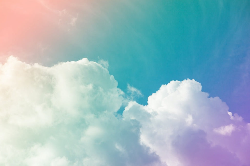 Fluffy white clouds against a vibrant Decor2Go Rainbow Sky Wallpaper Mural with a gradient of blue, pink, and orange colors, giving a dreamy and colorful backdrop perfect for bedrooms.