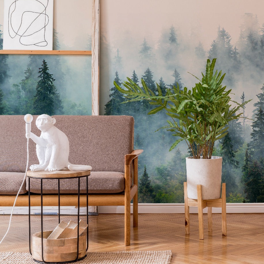 A cozy living room corner featuring a grey sofa with a white monkey-shaped lamp on an adjacent table, a plant in a concrete planter, local craftsmanship wooden stool, and a Decor2Go Wallpaper Mural of Reaching Tree Tops.