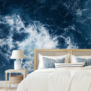 Bedroom - A modern bedroom featuring a queen-sized bed with white and blue bedding between two side tables, each with a lamp, against a Decor2Go Wallpaper Mural of Realm of Poseidon swirling blue ocean waves.