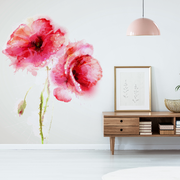 Living Room - A minimalist living room with a large Decor2Go Wallpaper Mural of Red Poppies Watercolor on a white wall, a wooden sideboard with books, a framed picture, and a plant beneath a hanging pink lamp.